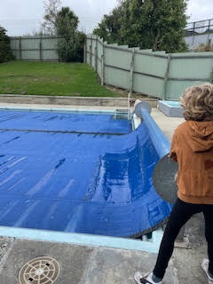 The pool cover being pulled back — the pool has sat dormant since the closure
